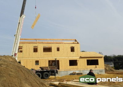 Crane lifts a roof panel onto a house with ridge beam and purlin